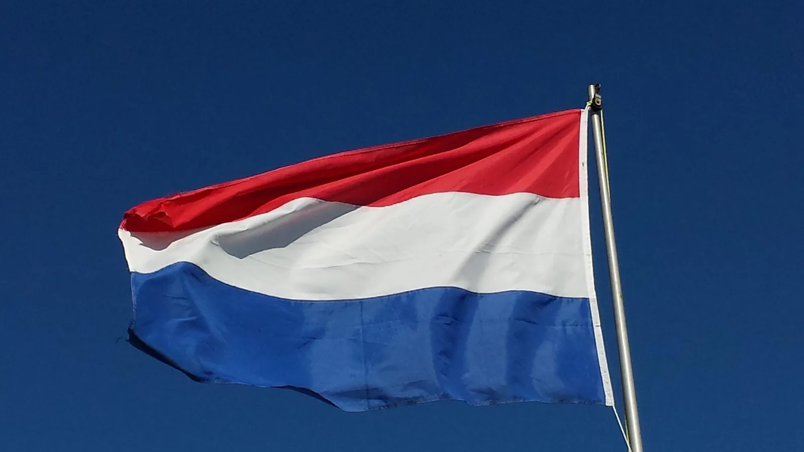 Nederlandse vlag aan een mast tegen een blauwe lucht